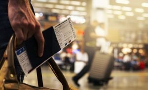 man holding a boardingpass, passport and luggage at an airport