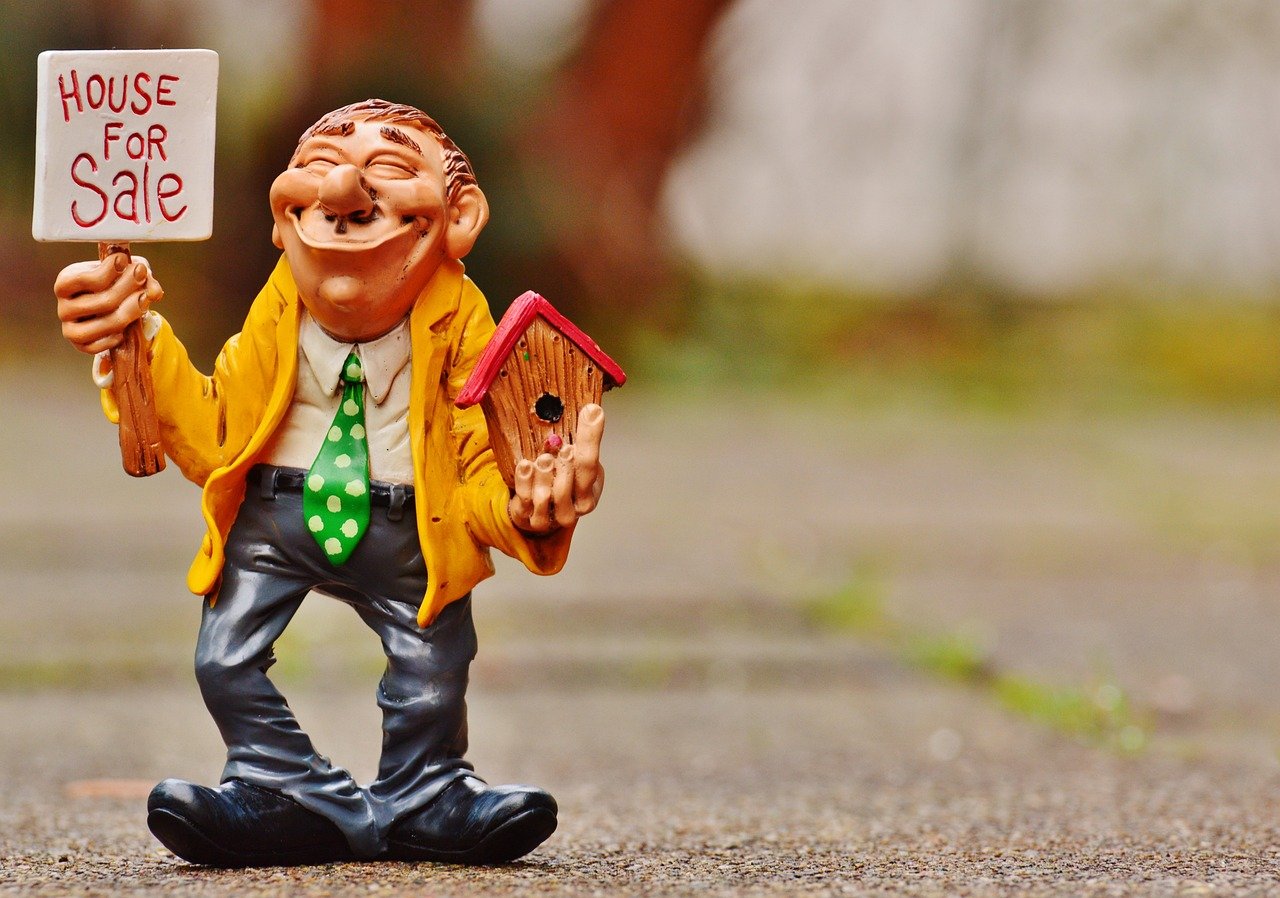 miniature doll showing a for sale sign for a house