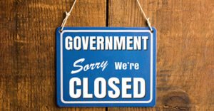 Government Shutdown concept. " Sorry we're closed " sign in blue and white, with the word "GOVERNMENT". Rustic wooden wall background.