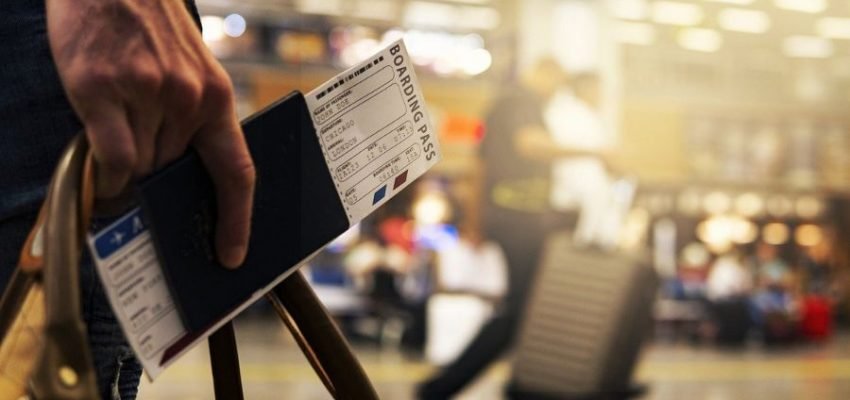 man holding a boardingpass, passport and luggage at an airport