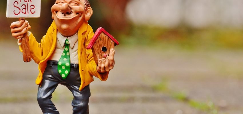 miniature doll showing a for sale sign for a house